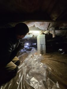 technician inspecting a crawl space for pest infestations using a flashlight